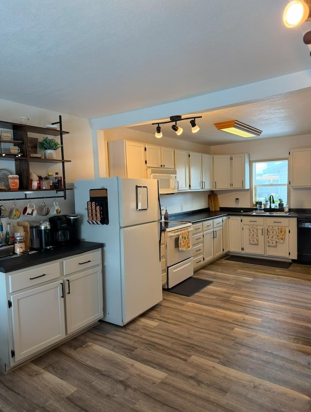 kitchen with dark countertops, white appliances, dark wood finished floors, and a sink