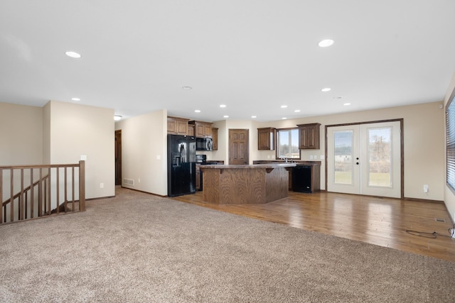 kitchen with french doors, wood-type flooring, black appliances, a kitchen island, and a breakfast bar