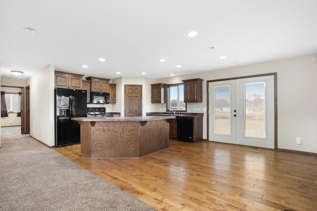 kitchen with light wood-type flooring, black appliances, a breakfast bar, and a center island