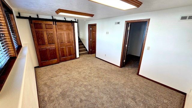 unfurnished bedroom with carpet flooring, a barn door, and a textured ceiling