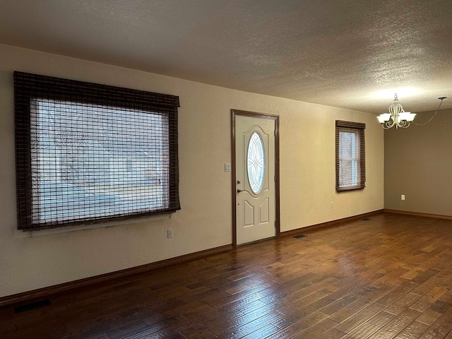 foyer entrance featuring a textured ceiling, dark hardwood / wood-style floors, and an inviting chandelier