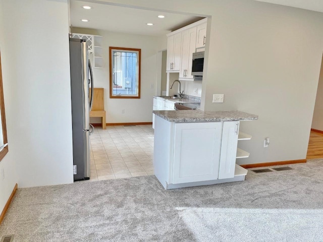 kitchen featuring kitchen peninsula, white cabinetry, stainless steel appliances, and light carpet