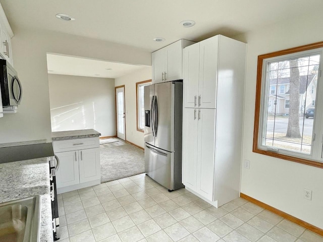 kitchen featuring white cabinetry, light tile patterned floors, stainless steel appliances, and light stone counters