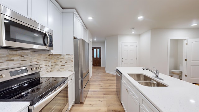 kitchen featuring white cabinetry, sink, stainless steel appliances, tasteful backsplash, and light wood-type flooring