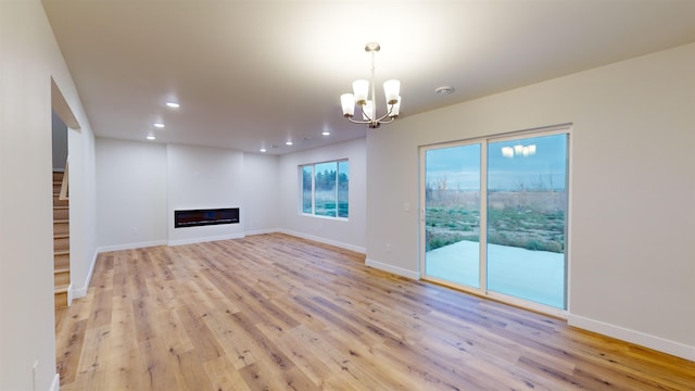 unfurnished living room featuring a notable chandelier and light wood-type flooring