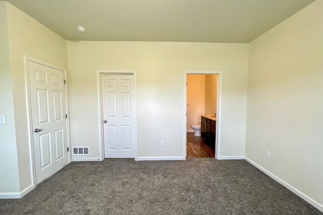 unfurnished bedroom with connected bathroom and dark carpet