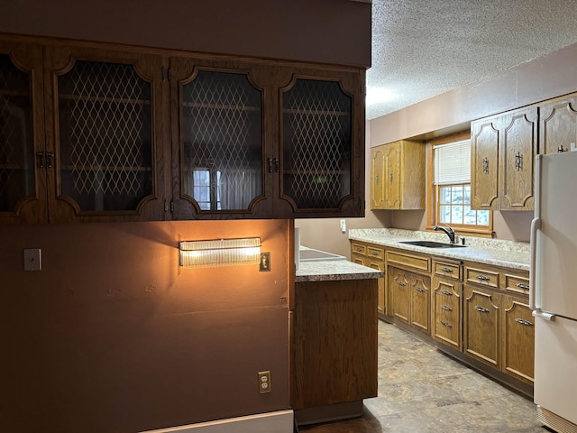 1107 SE 2nd St, Minot, ND 58701 - kitchen featuring freestanding refrigerator, a sink, light countertops, a textured ceiling, and brown cabinetry