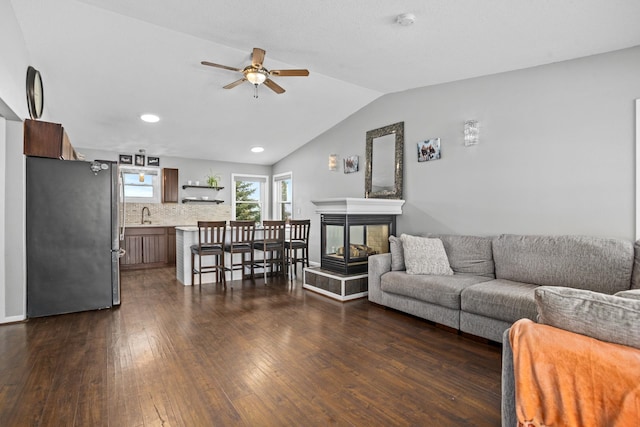 living room with ceiling fan, sink, a multi sided fireplace, dark hardwood / wood-style floors, and lofted ceiling