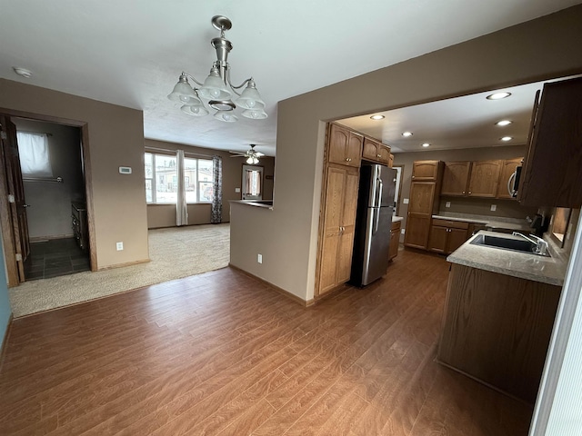 kitchen with sink, stainless steel appliances, pendant lighting, wood-type flooring, and ceiling fan with notable chandelier