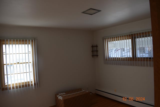 empty room with hardwood / wood-style floors, plenty of natural light, and a baseboard heating unit