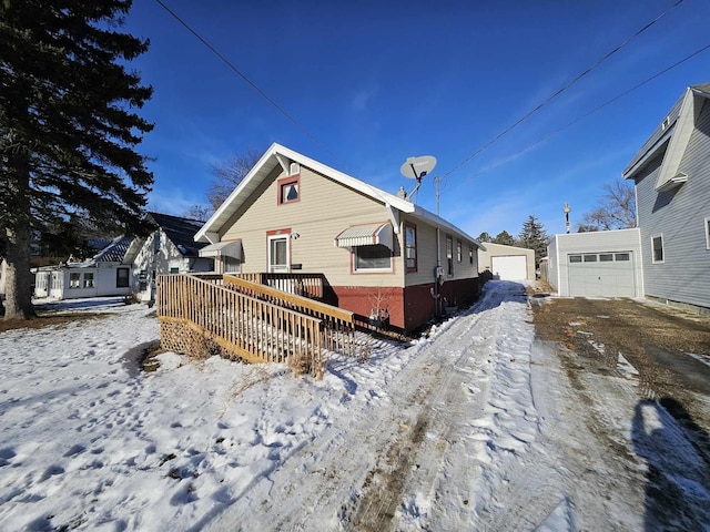 snow covered property featuring a garage, an outdoor structure, and a wooden deck