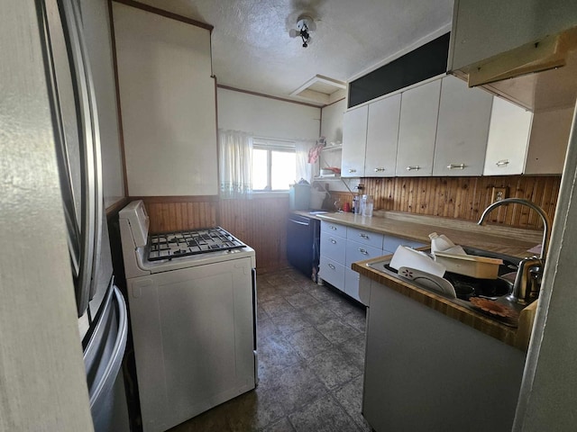 kitchen featuring stainless steel fridge, white gas range oven, white cabinetry, and wooden walls