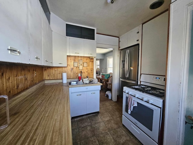 kitchen with wood walls, white cabinetry, stainless steel refrigerator with ice dispenser, and white range with gas cooktop