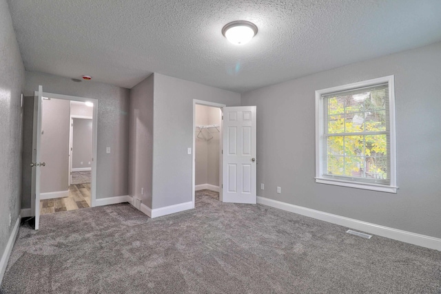 unfurnished bedroom featuring a walk in closet, a closet, carpet floors, and a textured ceiling