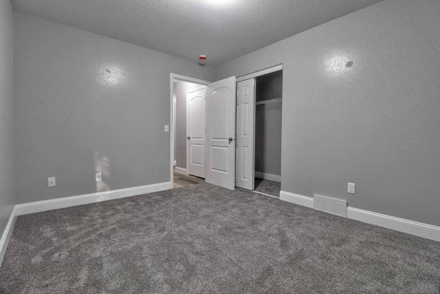 unfurnished bedroom with dark colored carpet, a textured ceiling, and a closet