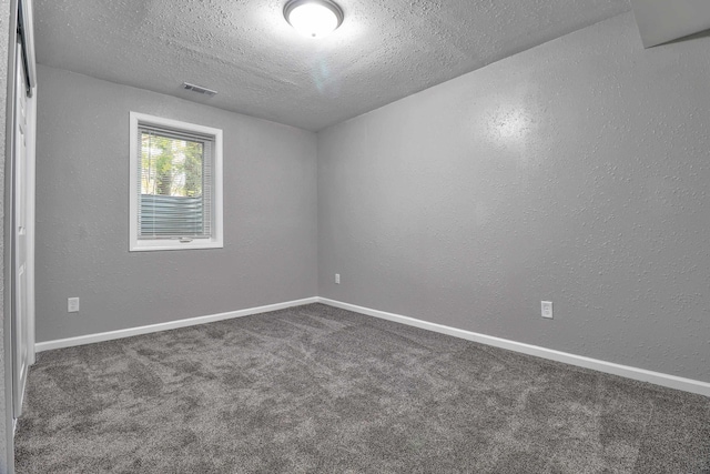 spare room featuring dark carpet and a textured ceiling