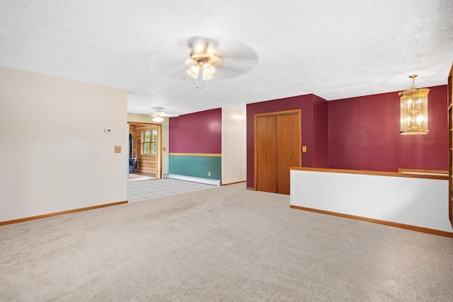 carpeted spare room featuring ceiling fan with notable chandelier and a textured ceiling