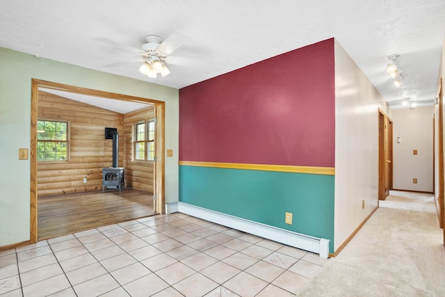 spare room with ceiling fan, a baseboard radiator, light hardwood / wood-style flooring, a wood stove, and lofted ceiling