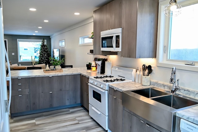 kitchen featuring kitchen peninsula, white appliances, sink, pendant lighting, and light hardwood / wood-style floors