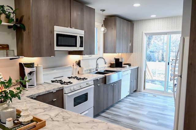 kitchen featuring light wood-type flooring, light stone counters, white appliances, sink, and decorative light fixtures