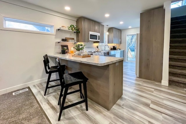 kitchen with kitchen peninsula, light wood-type flooring, a kitchen bar, and plenty of natural light