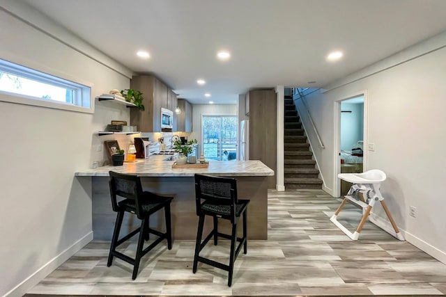 kitchen with a kitchen bar, kitchen peninsula, stainless steel microwave, and light wood-type flooring