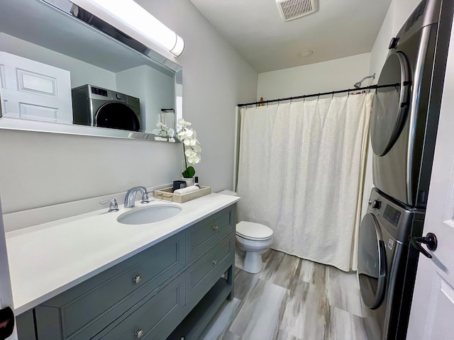 bathroom featuring toilet, vanity, stacked washer / drying machine, and hardwood / wood-style flooring