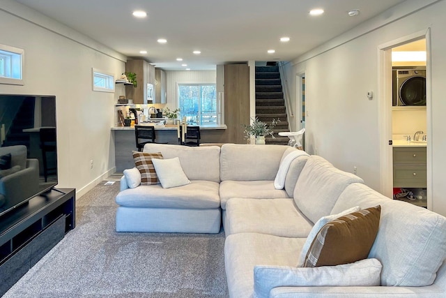 carpeted living room with stacked washer and clothes dryer and sink