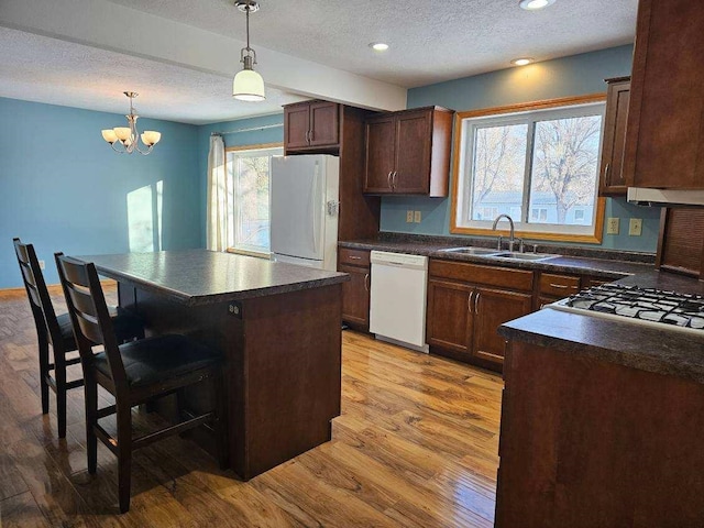 kitchen with white appliances, an inviting chandelier, sink, a kitchen island, and light hardwood / wood-style floors