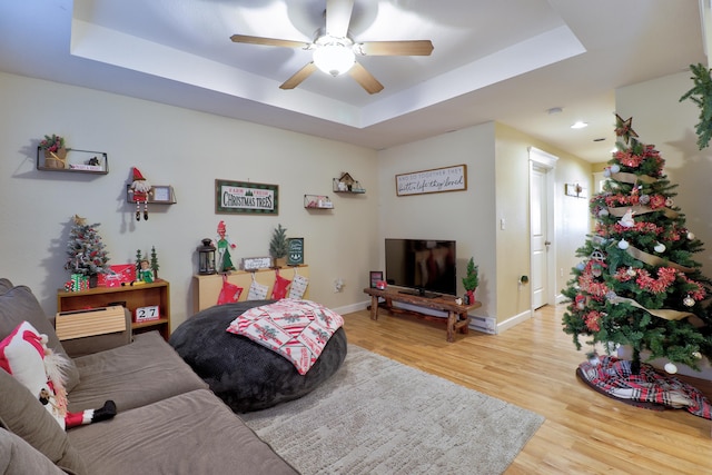 living room with hardwood / wood-style floors, a tray ceiling, and ceiling fan