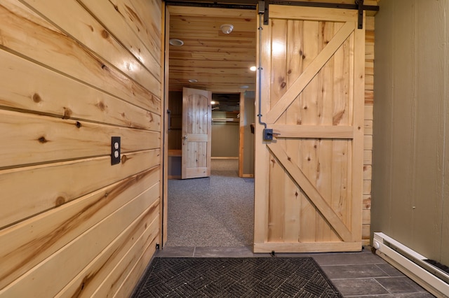 hall featuring wood walls, a barn door, baseboard heating, and dark carpet