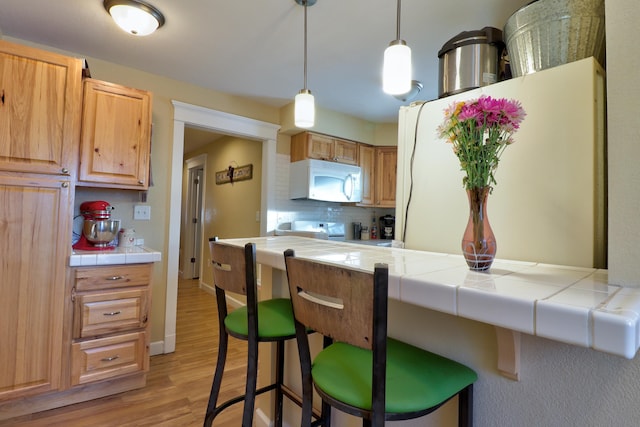 kitchen featuring tile counters, a kitchen breakfast bar, white appliances, decorative backsplash, and light wood-type flooring