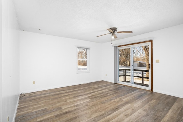 unfurnished room with a wealth of natural light, ceiling fan, dark wood-type flooring, and a textured ceiling