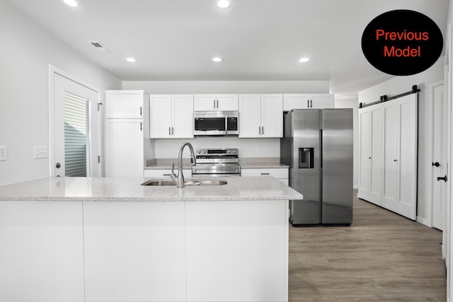 kitchen featuring white cabinets, sink, stainless steel appliances, and a kitchen island with sink