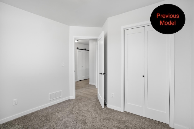 unfurnished bedroom with light carpet and a barn door