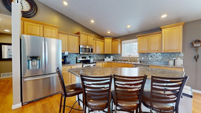 kitchen featuring sink, a center island, vaulted ceiling, appliances with stainless steel finishes, and light wood-type flooring