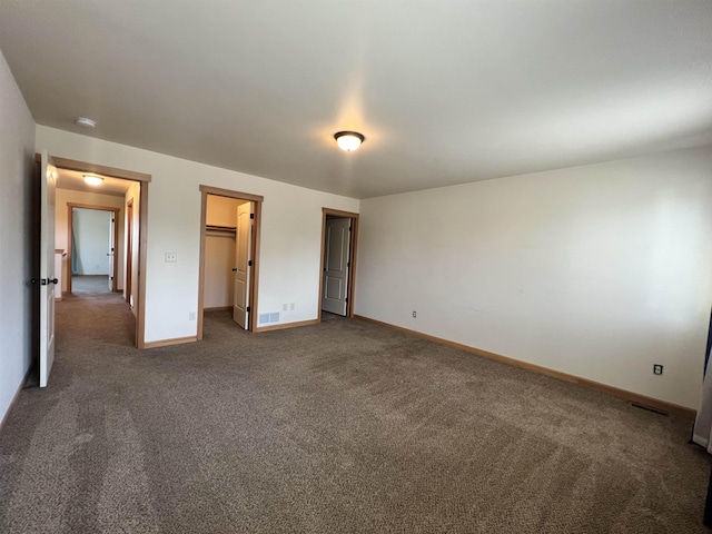 unfurnished bedroom with a walk in closet, dark carpet, and a closet