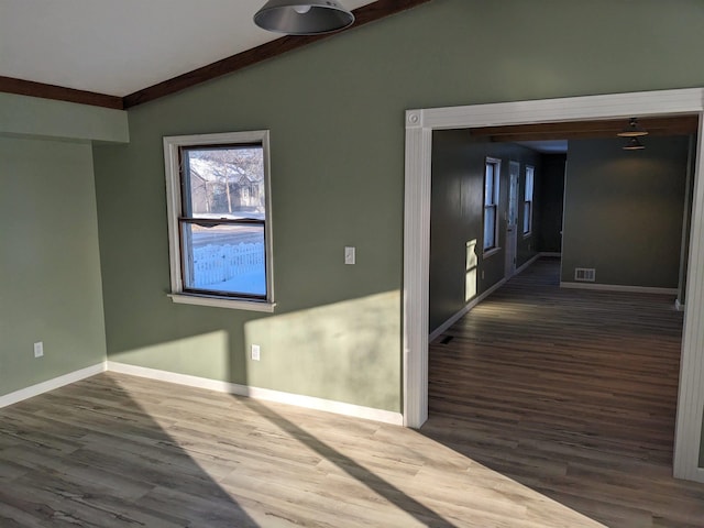 empty room featuring dark wood-type flooring, vaulted ceiling, and ornamental molding