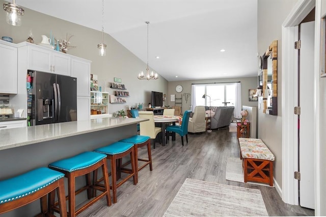 kitchen featuring fridge with ice dispenser, white cabinets, hardwood / wood-style floors, hanging light fixtures, and a breakfast bar area