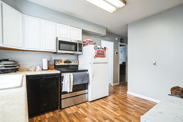 kitchen with appliances with stainless steel finishes, light hardwood / wood-style floors, white cabinetry, and sink