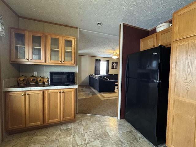 kitchen featuring a textured ceiling, ceiling fan, crown molding, black appliances, and tile counters