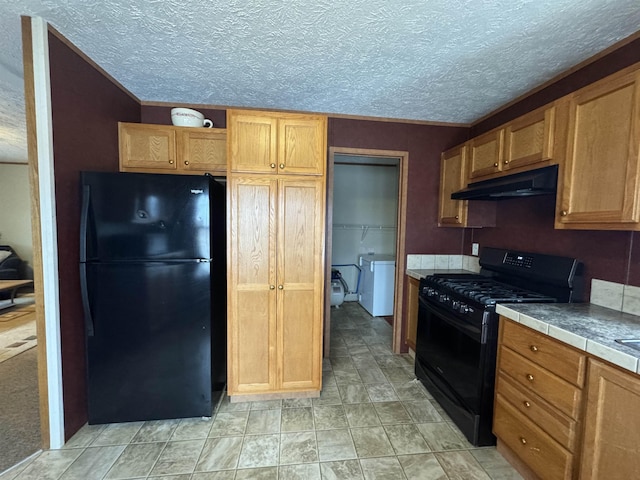 kitchen featuring black appliances, independent washer and dryer, a textured ceiling, and tile countertops