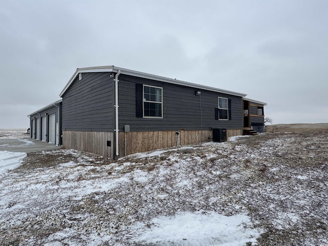 snow covered back of property with central air condition unit and a garage