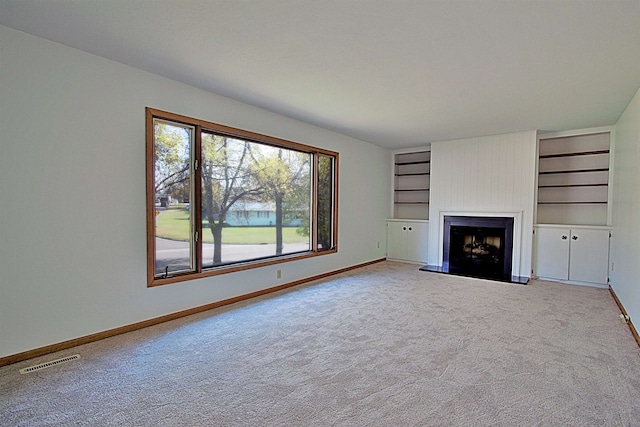 unfurnished living room featuring a fireplace, built in shelves, and carpet flooring