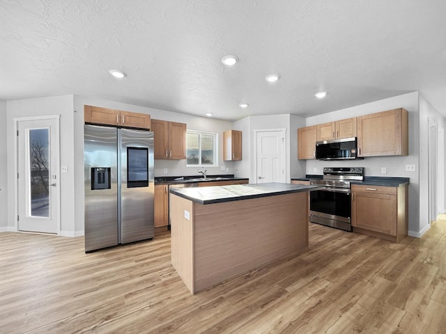 kitchen featuring sink, stainless steel appliances, a textured ceiling, a kitchen island, and light wood-type flooring