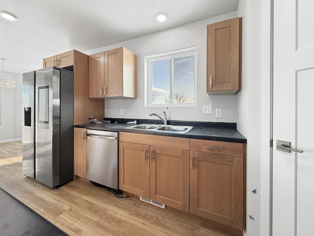 kitchen with pendant lighting, sink, stainless steel appliances, and light hardwood / wood-style flooring