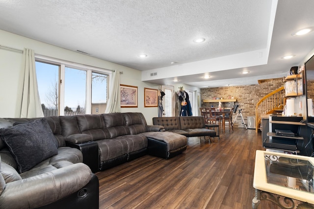 living room with a textured ceiling, dark wood-type flooring, and brick wall