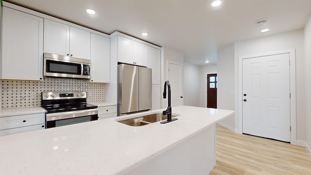 kitchen with backsplash, sink, light wood-type flooring, appliances with stainless steel finishes, and white cabinetry