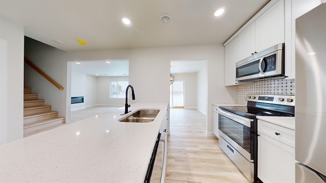 kitchen featuring light stone countertops, stainless steel appliances, white cabinetry, and sink