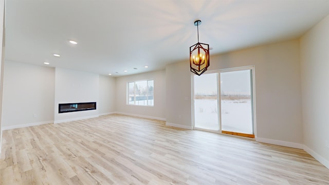 unfurnished living room featuring an inviting chandelier and light hardwood / wood-style flooring